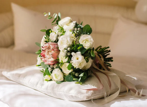 Pembe protea ve ranunculus çiçekleri ile klasik beyaz ve yeşil gelin buketi yatakta yatıyor. Klasik düğün konsepti.