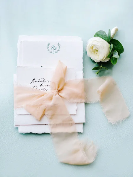 Wedding calligraphy on pale blue background with peach ribbon and a flower in white and green tones. Wedding decoration with invitation. Wedding blog concept. Handwriting calligraphy.