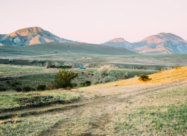 Çimenli çimenler, pembe gökyüzü, mavi araba ile yeşil dağ manzara. Sonbaharda Kırım