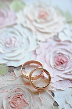 Çiçeklerle boyanmış arka planda yazılı klasik bir alyans seti. Davetiye kartı. Altın alyanslar üst manzara, düz yatış. Yumuşak odak, güzel bokeh, bulanık arkaplan. Sevgililer Günü kartı.