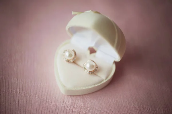 White earl earrings in a box for jewelry. Gift for the beloved lady on the anniversary, wedding or birthday on the dust pink background. Elegance classic rosy gold pearl bridal earrings.