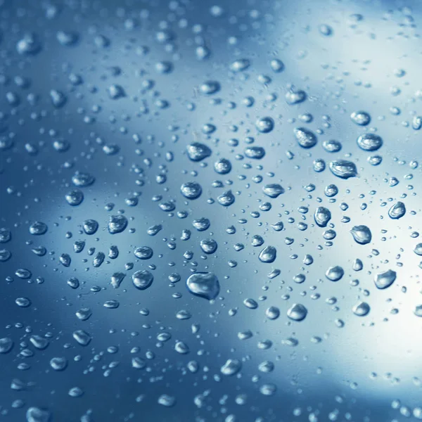 mavi arka plan üzerinde su damlaları, yakın çekim. Pencere camına yağmur damlaları