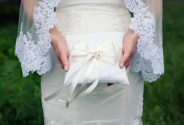 花嫁の手に結婚指輪と白の枕 古典的な金の結婚指輪を彼女の手で保持している白いウェディング ドレスと長いベールの花嫁 — ストック写真