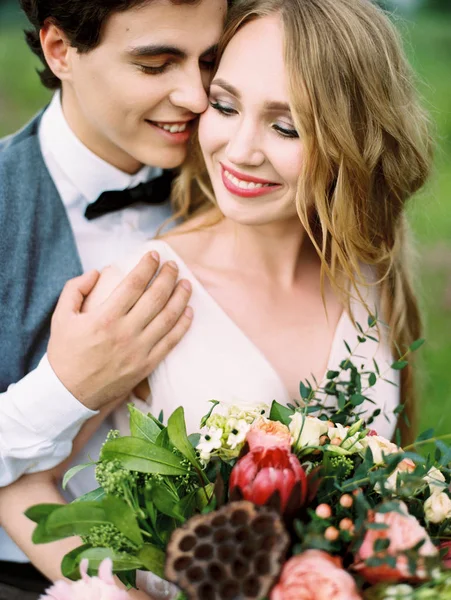 outdoor portrait of happy newlyweds, smiling bride holding beautiful bouquet