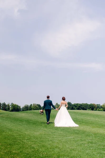 緑の芝生で歩く幸せな美しい新婚夫婦の屋外のポートレート — ストック写真