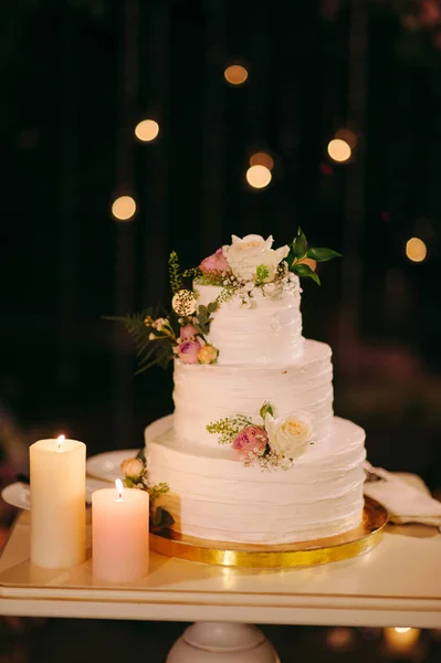 white wedding cake decorated with flowers and candles on table