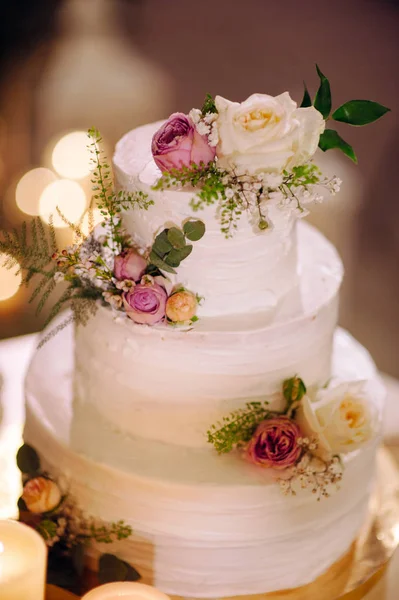 White three tiered cake decorated with fresh flowers. Traditional creamy cake at wedding party.