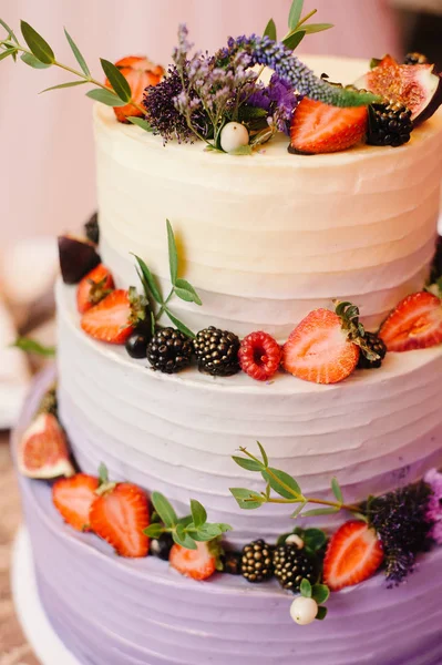 Bright three tiered wedding cake. White creamy cake decorated with fesh fruits, berries and flowers.