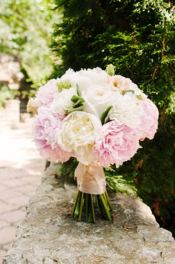 Classic wedding bouquet with tender flowers stands on stone