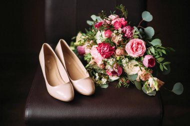 Pembe ve kırmızı çiçekli organik düğün buketi ve koyu arkaplanda fildişi düğün ayakkabıları.