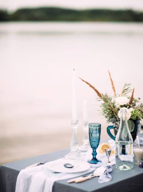 Deniz sahilinde şık bir masa. Vazoda narin çiçekler olan düğün buketi.