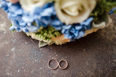 Altın alyanslar, içinde sonsuz aşk konsepti ve düğün buketi olan eski taş bir masanın üzerinde duruyor. 