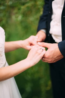 Düğün konsepti. Gelin ve damat yeşil çimen arka planında el ele tutuşuyorlar. Evlilik yüzükleri.