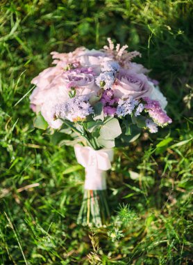 Mor gelin buketi güneşte yemyeşil çimlerde, düz yerde. Yumuşak leylak çiçekli yuvarlak düğün buketi