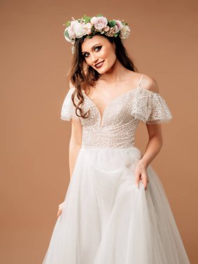 Boho düğün tarzı. Beyaz bir gelinlik içinde, kolları ve bej arkaplanda çiçeklerle süslenmiş güzel bir gelin..