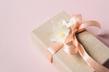 Üzerinde yasemin çiçekleri ve pembe masa manzaralı hediye kutusu olan bahar kompozisyonu. Doğum günü, kadın ya da anneler günü için tebrik kartı. Düz yatıyordu. Bir fiyonk, çiçekler ve keten kumaşla güzel bir hediye paketi. paket kağıdı..