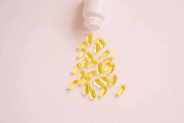 Birçok tablet plastik bir konteynere dökülür. Hastalık tedavisi kavramı. Yakın plan, pembe tarafsız arkaplan manzaralı. Vitamin tedavisi, balık yağı, D vitamini..