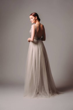 Nedimenin toz grisi içinde görünüşü. Stüdyodaki gri arka planda parıldayan parlak elbiseli kızıl saçlı genç bir kadının güzel portresi. Arka görünüm.