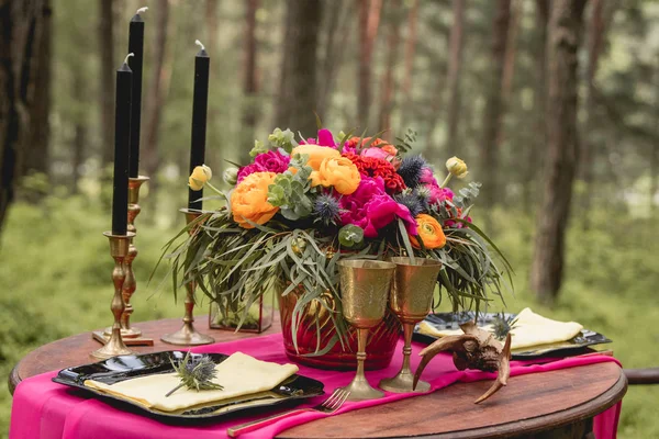 Decoração. Detalhes. Composição. Decorações de casamento. Na mesa de madeira na floresta há um arranjo de flores com flores vermelhas, cor-de-rosa e vegetação, velas, estatuetas — Fotografia de Stock