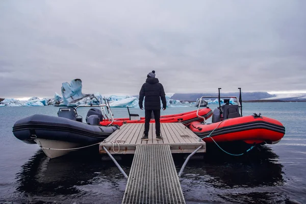 The man standing on pier in winter. Stylish winter clothes. Icebergs in Jokulsarlon lagoon