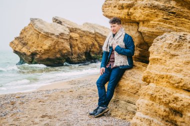 Dalgalar ile güzel bir denize karşı bir kaya yakınında Gezgin adam, dünya çapında harika bir yolculuk sırasında sakin bir okyanus yakınında poz şık bir hipster çocuk