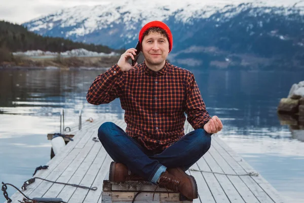 Traveler man talking on mobile phone. Tourist in a yellow backpack standing on a background of a mountain and a lake. Traveler walks, smiling man calling friends. Telephone conversation.