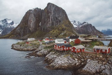 Arka planda deniz ve yüksek dağların önünde kırmızı balıkçı evleri ile Lofoten Adaları Klasik ve güzel manzara, Kuzey Avrupa, Norveç
