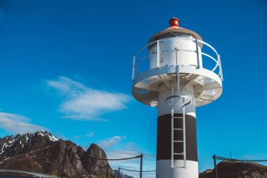 Dağların arkasındaki iskelede deniz feneri ve Lofoten Adaları 'ndaki mavi gökyüzü.