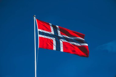 Mavi gökyüzüne karşı Norveç bayrağı. Rüzgar bulutsuz mavi gökyüzüne doğru eser.