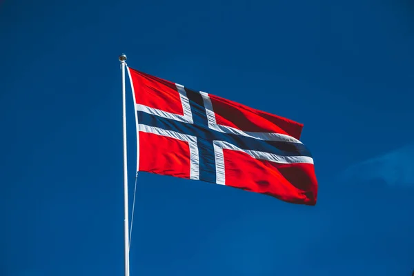 Mavi gökyüzüne karşı Norveç bayrağı. Rüzgar bulutsuz mavi gökyüzüne doğru eser.
