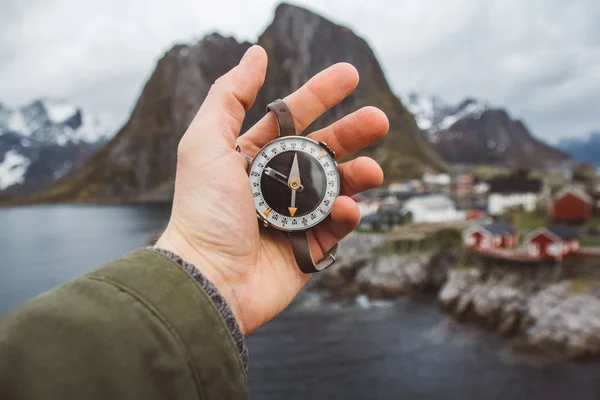 Beautiful male hand holds a magnetic compass against the background of the houses and mountains rocks over fjord landscape . The concept of finding yourself the way and the truth. — Stock Photo, Image