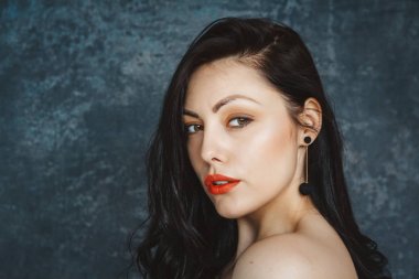 Siyah bir elbise giyen şık bir esmer kız moda portresi. Uzun saçlı, küpe giyen kadın. Gri arka planda ayarlama
