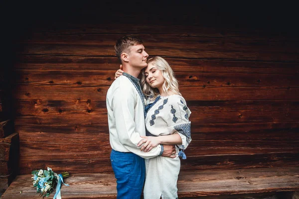 Couple de mariage incroyable dans une chemise brodée avec un bouquet de fleurs sur le fond d'une maison en bois — Photo