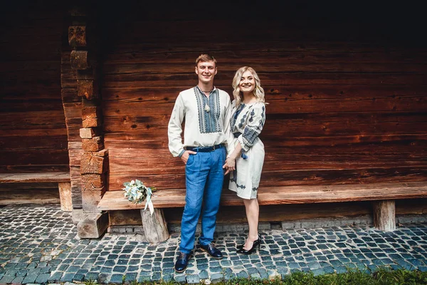 惊人的新婚夫妇在刺绣衬衫与一束鲜花的背景下, 一个木制的房子 — 图库照片