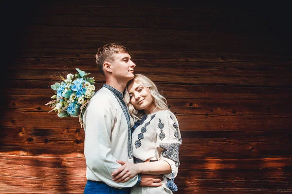 Casal incrível em uma camisa de bordados com um monte de flores no fundo de uma casa de madeira Imagens De Bancos De Imagens