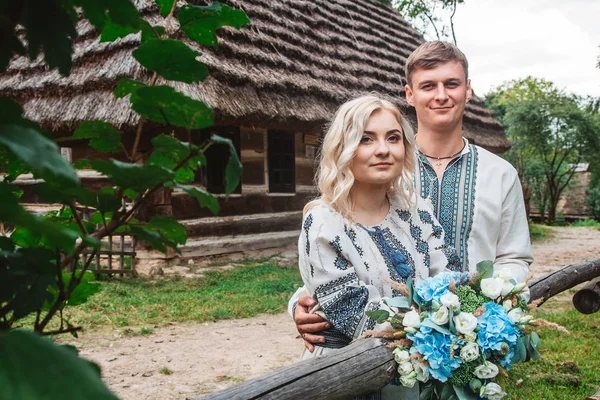 Couple de mariage incroyable dans une chemise brodée avec un bouquet de fleurs sur le fond d'une maison en bois — Photo