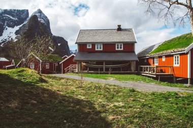 Arka planda deniz ve yüksek dağların önünde kırmızı balıkçı evleri ile Lofoten Adaları Klasik ve güzel manzara, Kuzey Avrupa, Norveç
