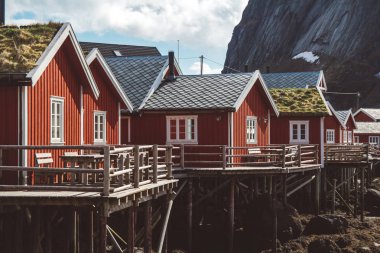Arka planda deniz ve yüksek dağların önünde kırmızı balıkçı evleri ile Lofoten Adaları Klasik ve güzel manzara, Kuzey Avrupa, Norveç
