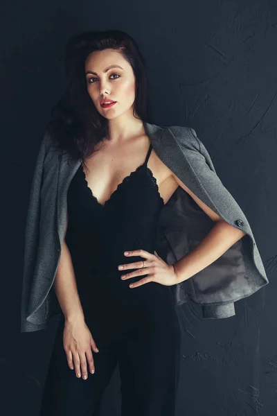 美しい若いビジネスウーマンスタジオは、黒い背景に撮影しました。カジュアルなダークグレーのジャケットで魅力的で自信に満ちた深刻なブルネットの女性 — ストック写真
