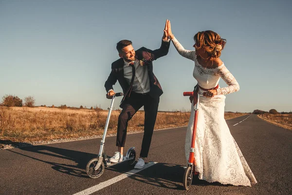 Gülümseyen düğün çifti gün batımında şehrin dışındaki yolda scooter 'a biniyor..