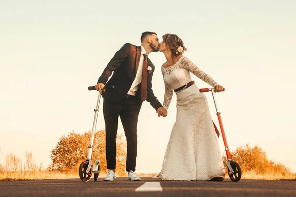 Couple de mariage embrasser sur scooters le long de la route en dehors de la ville au coucher du soleil . — Photo