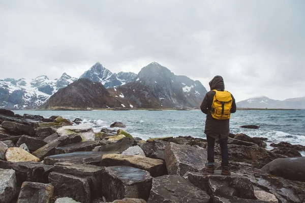 Podróżnik w żółtym plecaku stojący na skałach na tle morza i gór. Miejsce na wiadomości tekstowe lub treści promocyjne. Koncepcja stylu życia podróży. — Zdjęcie stockowe