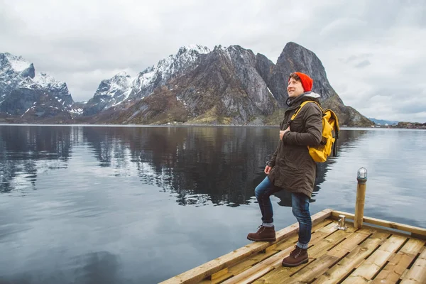 Hombre viajero con una mochila amarilla con un sombrero rojo de pie sobre el fondo del muelle de madera de montaña y lago. concepto de estilo de vida — Foto de Stock