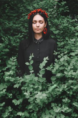 Gözleri siyah giysiler içinde ve arka planda kırmızı küpeler takmış güzel bir kız.
