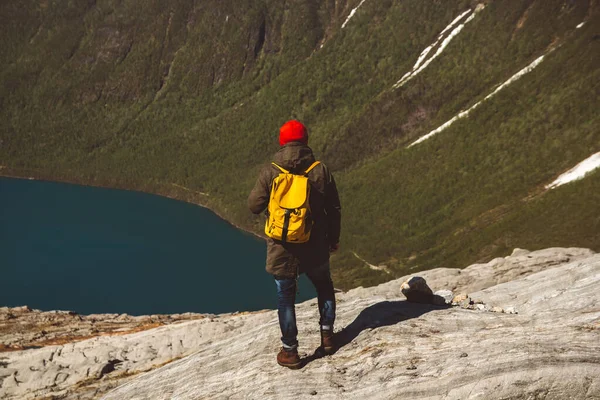 Reiziger met een gele rugzak met een rode hoed op op een rots op de achtergrond van berg en meer. Ruimte voor uw sms-bericht of promotionele inhoud. Reizen lifestyle concept. Schiet. — Stockfoto