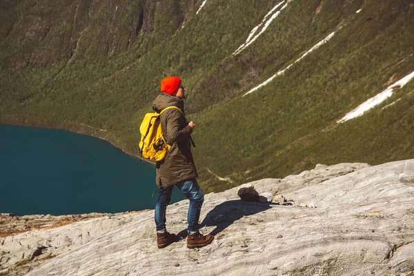 Reiziger met een gele rugzak met een rode hoed op op een rots op de achtergrond van berg en meer. Ruimte voor uw sms-bericht of promotionele inhoud. Reizen lifestyle concept. Schiet. — Stockfoto