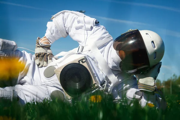 Futuristic astronaut in a helmet sits on a green lawn among flowers.