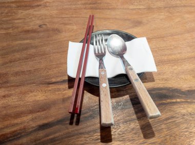 Çatal bıçak takımı, kağıt üzerinde yemek çubukları, ahşap bir masaya yerleştirilmiş..