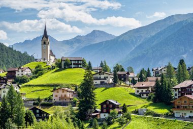 Beautiful Schmitten village at Albula pass in Grisons, Graubuenden, Switzerland with view of houses on green grassy hills, a lovely church on hilltop and majestic mountains in background clipart