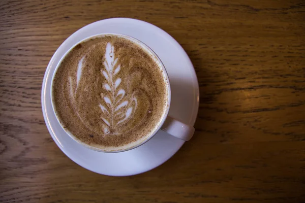 Cup of cappuccino with a painted flower on a wooden texture